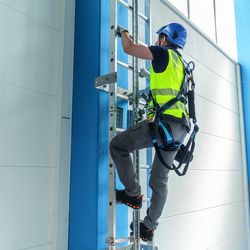 Industriekletterer steigt eine Steigleiter hoch, an die er durch die Absturzsicherung von ZARGES befestigt und gesichert ist