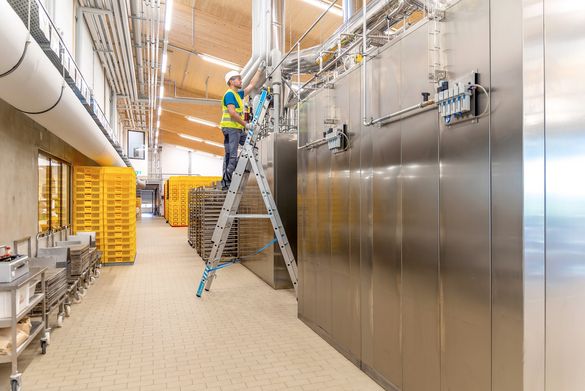 Ein Mann mit Warnweste und Helm steht auf der Mehrzweckleiter Skymaster Plus X