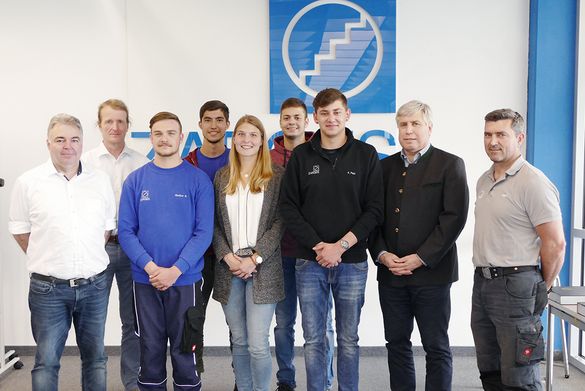 ZARGES Azubi Absolventen mit Ausbildern und Geschäftsführer vor einem ZARGES Logo