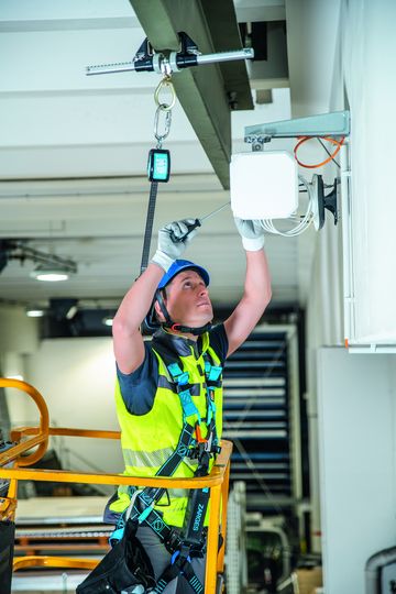 Ein Elektriker führt seine Arbeit auf einer Arbeitsbühne aus, während er von der speziellen Absturzsicherung für Stahlbauten gesichert wird