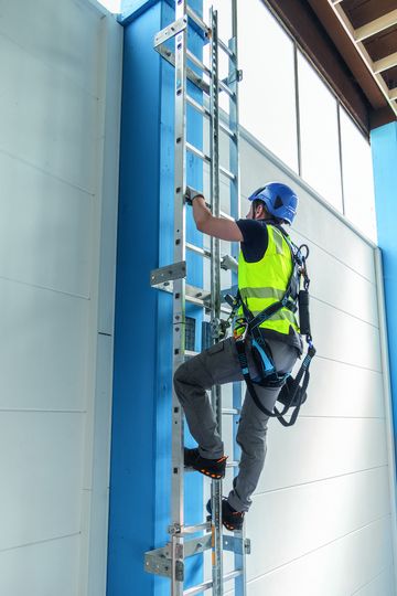 Industriekletterer steigt eine Steigleiter hoch, an die er durch die Absturzsicherung von ZARGES befestigt und gesichert ist