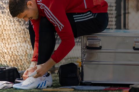 Ein Fußballspieler zieht sich seine Schuhe an, während er auf einer ZARGES Box sitzt, die als Trikotbox dient.